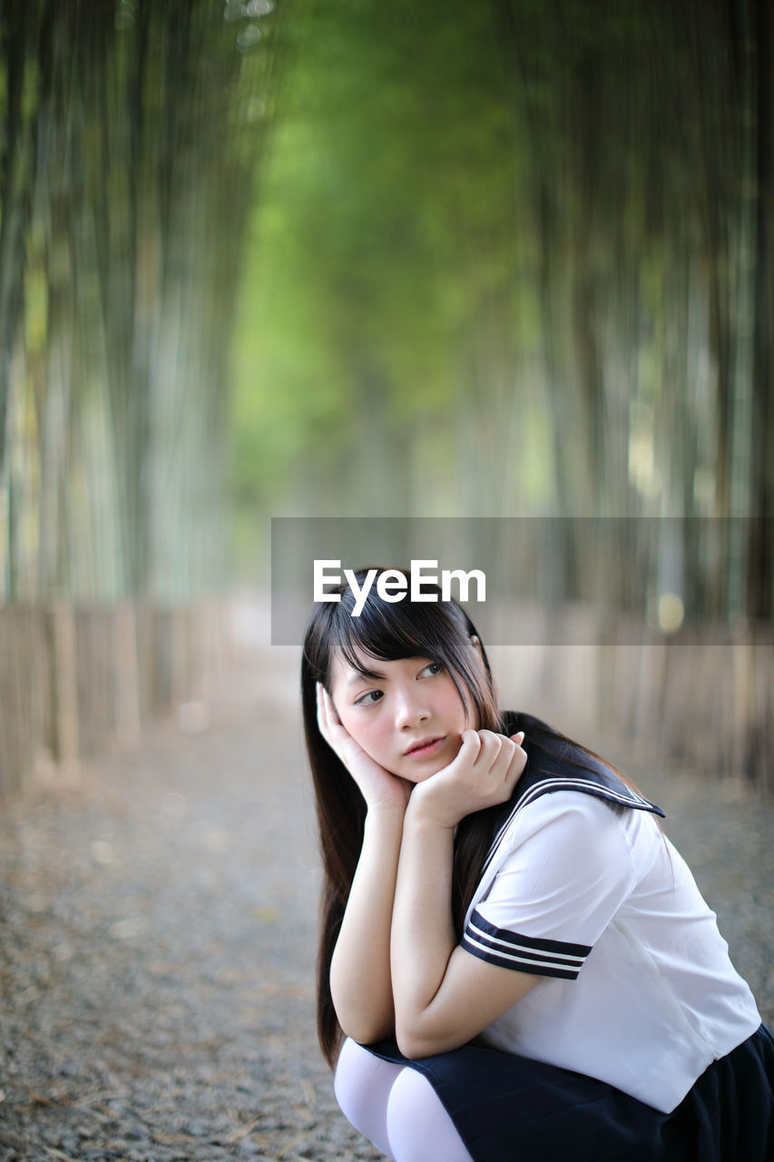 Side view of young woman crouching in bamboo groove