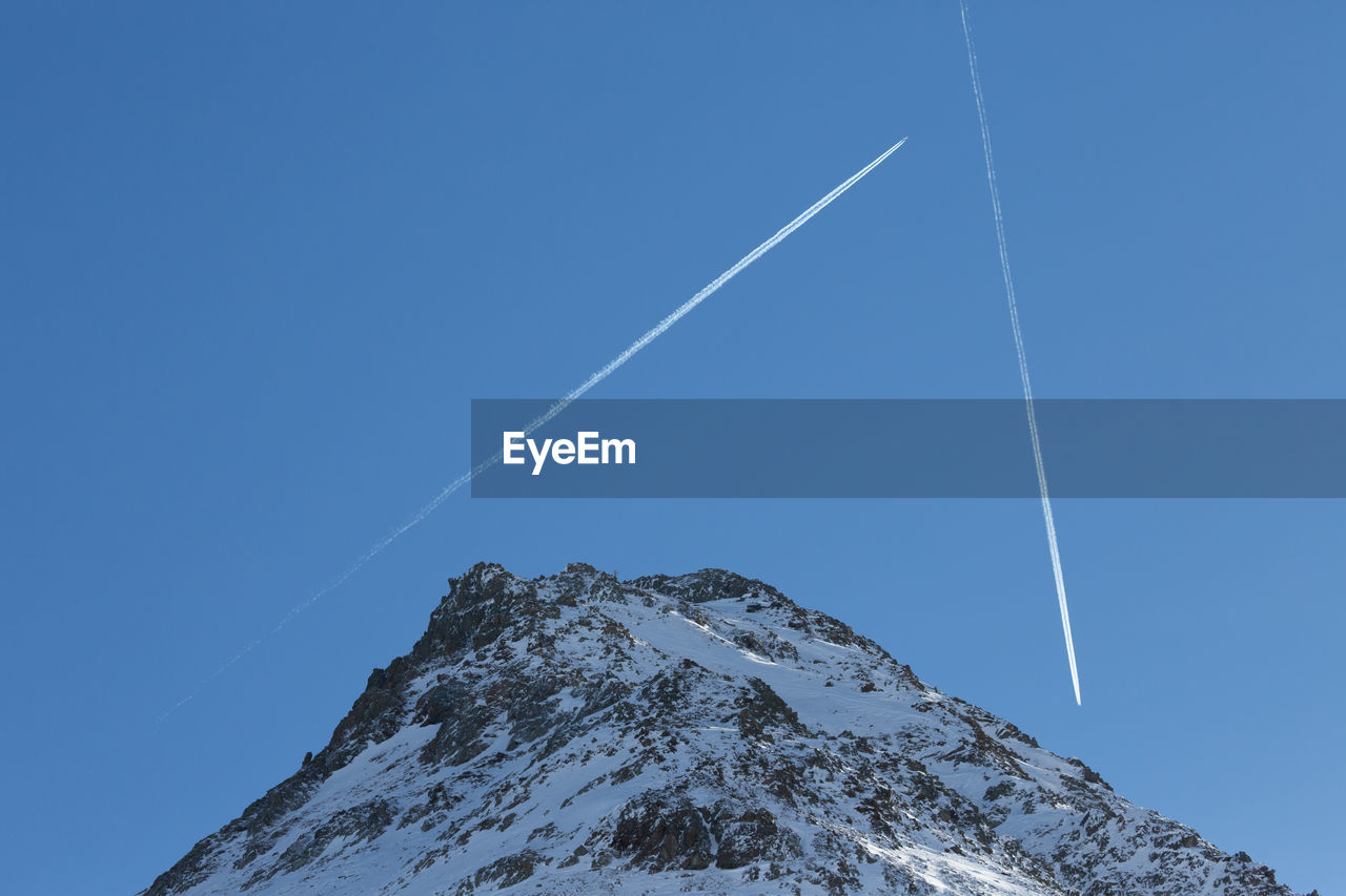 Low angle view of vapor trail and the european alps against clear blue sky