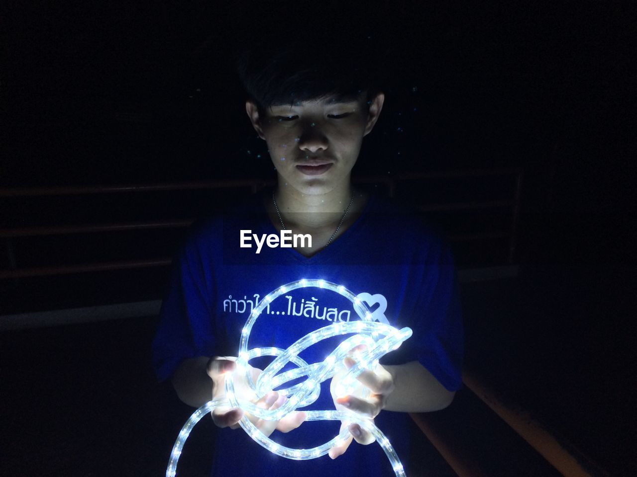 Young man holding illuminated lighting equipment while standing on balcony at night