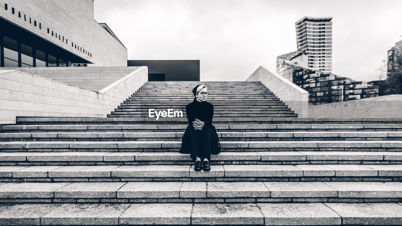 Thoughtful woman sitting on staircase against sky