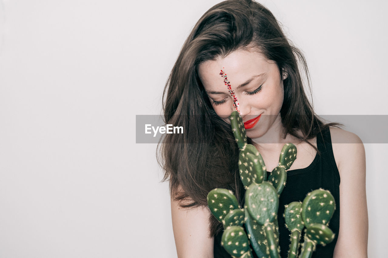 Close-up of woman with cactus against white background