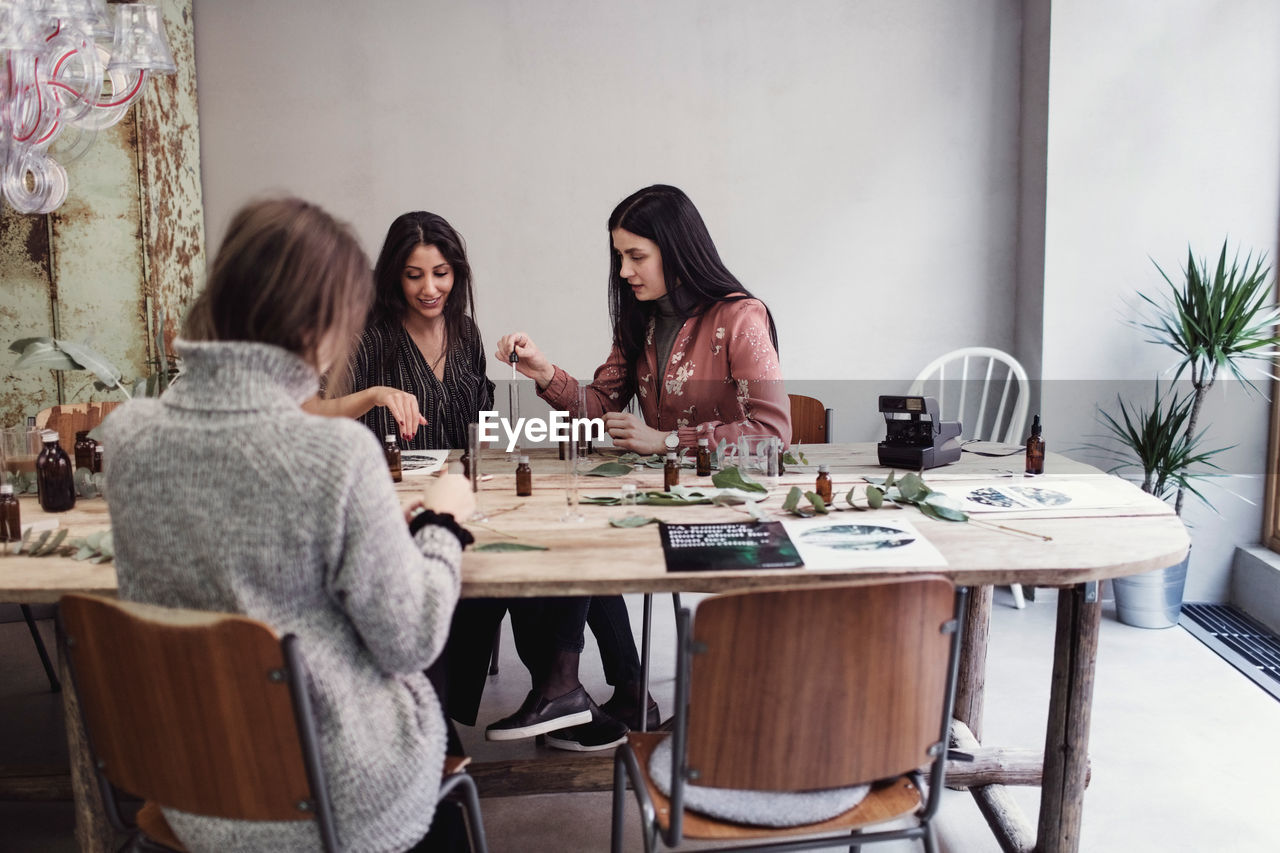 Female colleagues preparing perfume while sitting at table in workshop