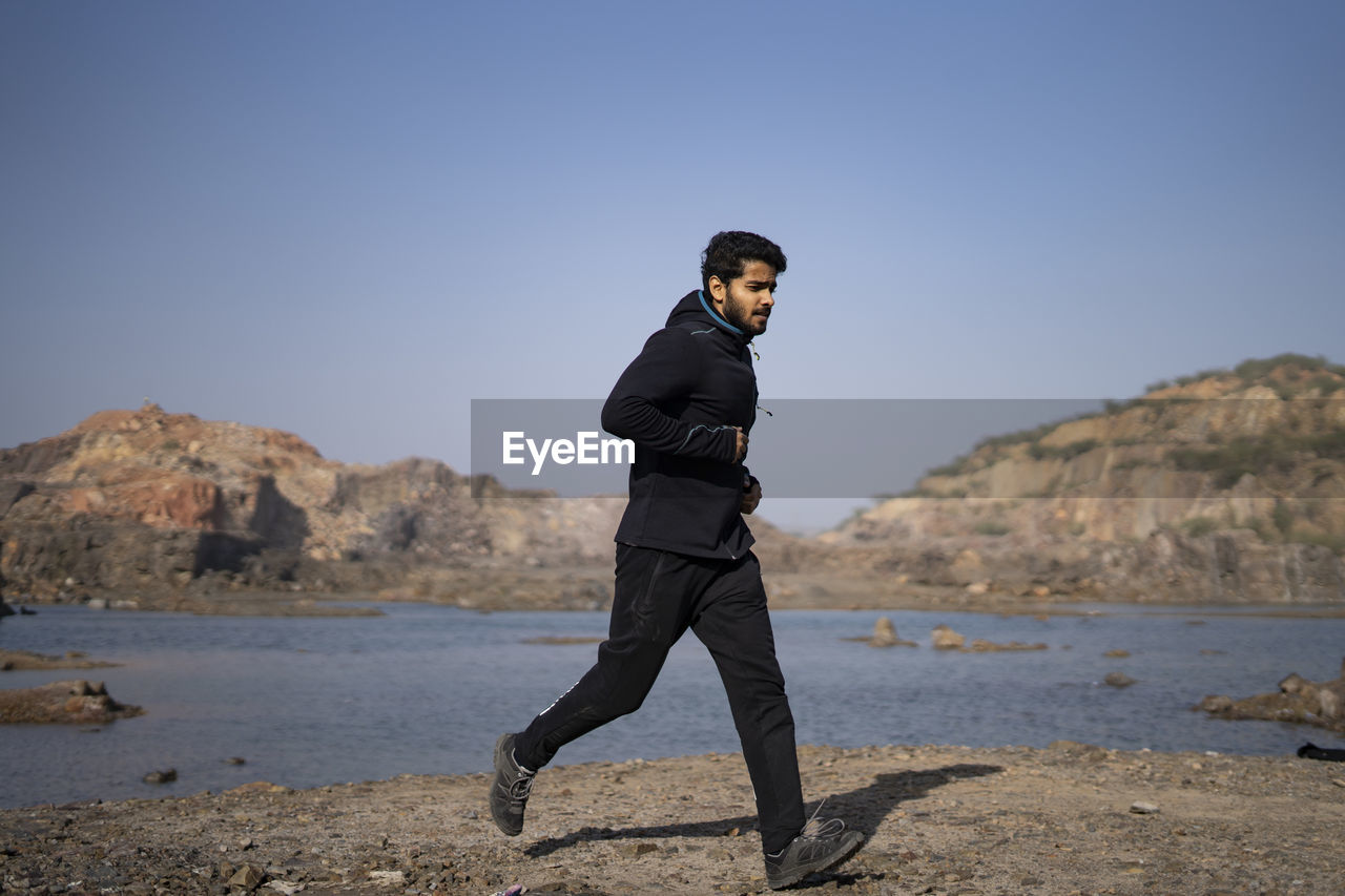 Young indian fit boy jogging in the morning near a lake situation in middle of a mountain area.