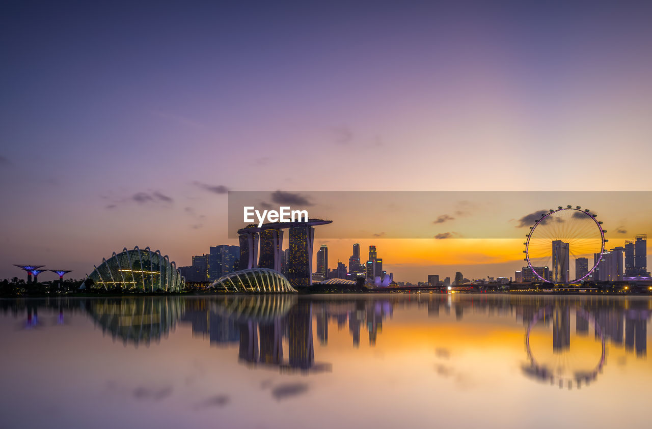 Reflection of buildings in river against sky during sunset