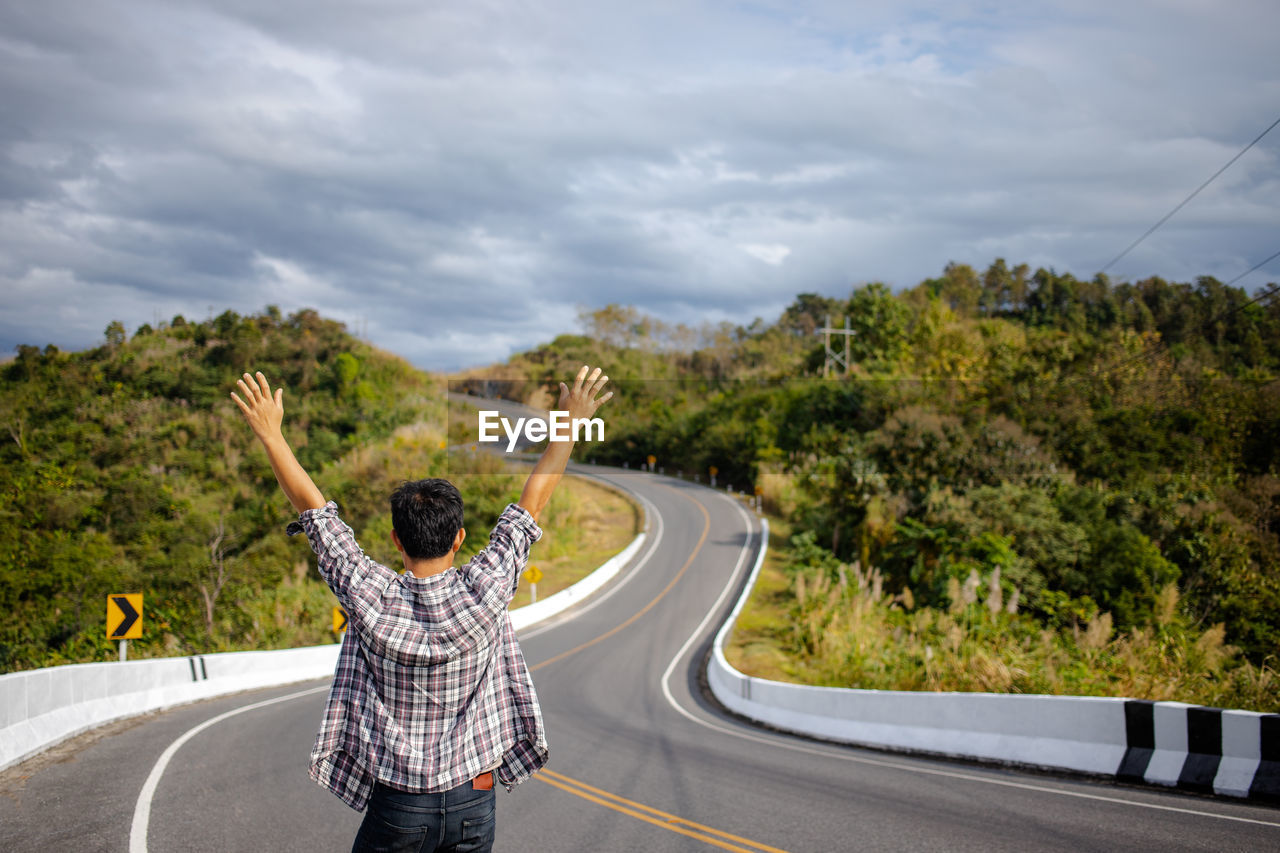 Rear view of man with arms raised standing on road against sky