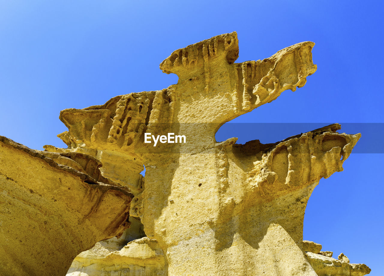 Low angle view of las gredas limestone cliffs against blue sky