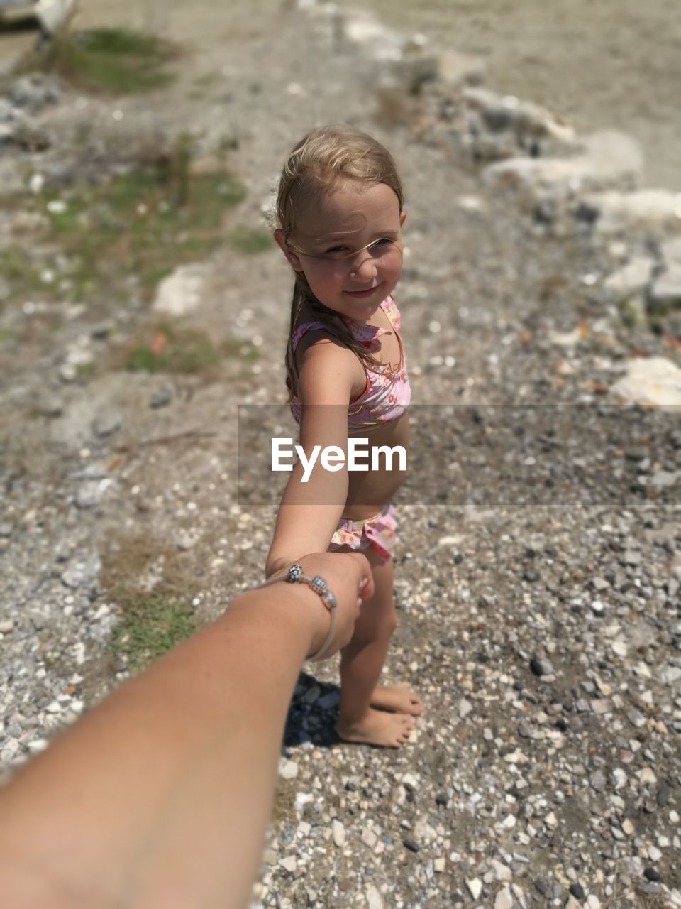 Cute girl holding cropped hand of mother at beach