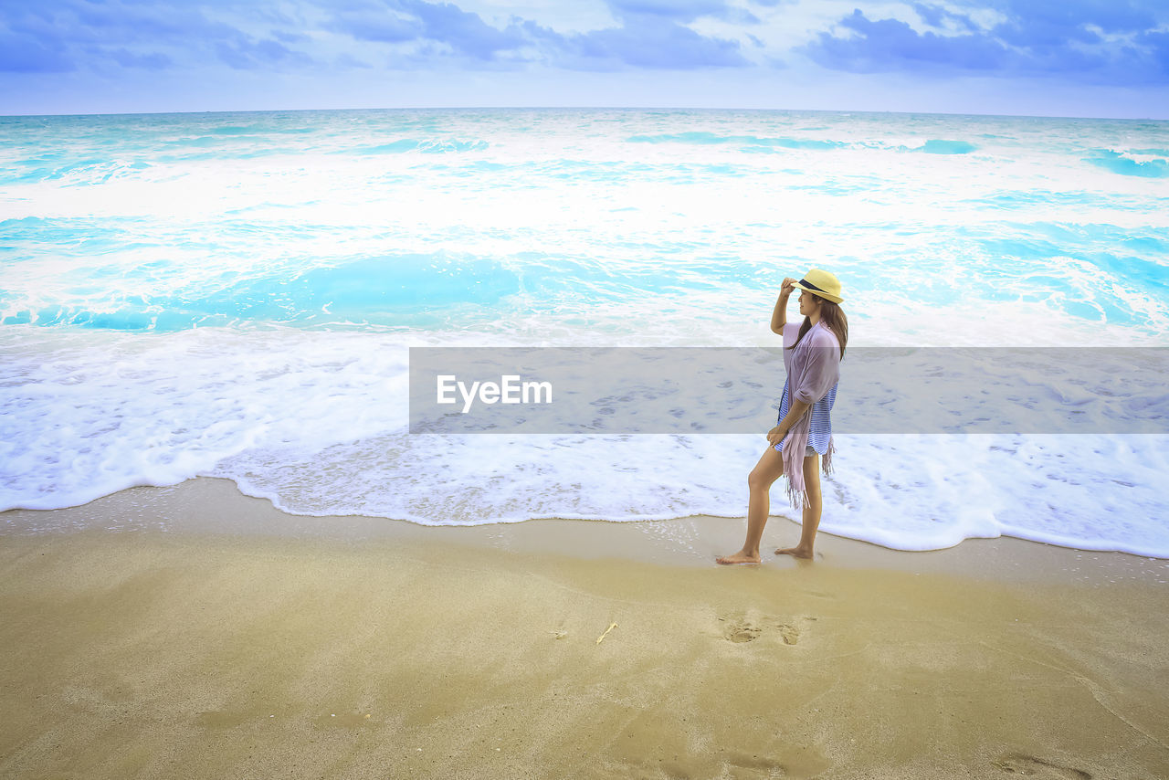 FULL LENGTH OF WOMAN STANDING ON BEACH AGAINST SKY