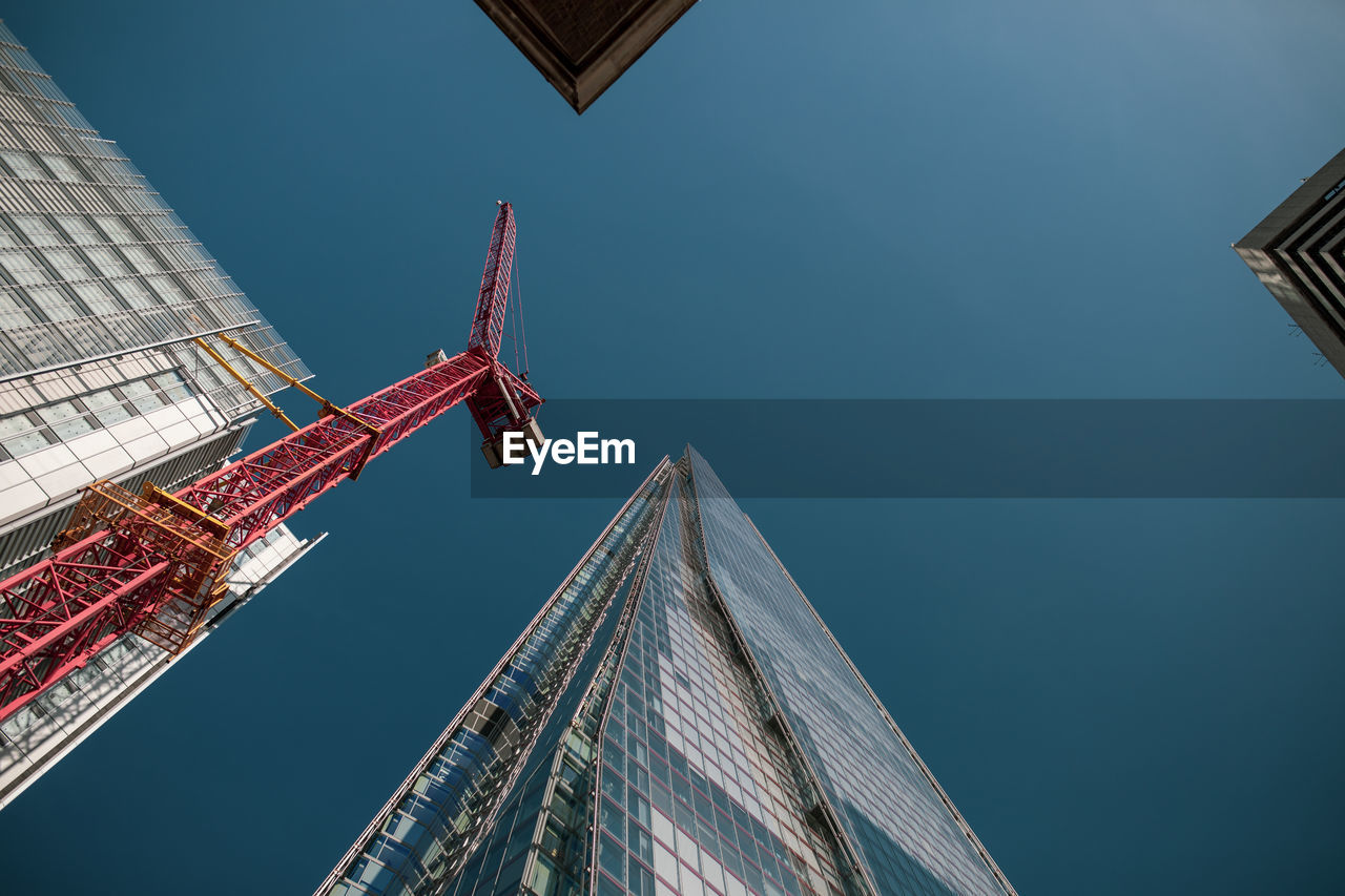 LOW ANGLE VIEW OF CRANE BY BUILDINGS AGAINST SKY