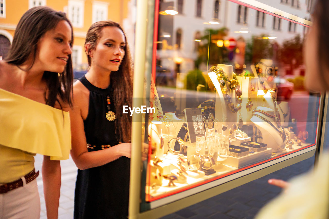 Female friends looking at store window with jewelry 