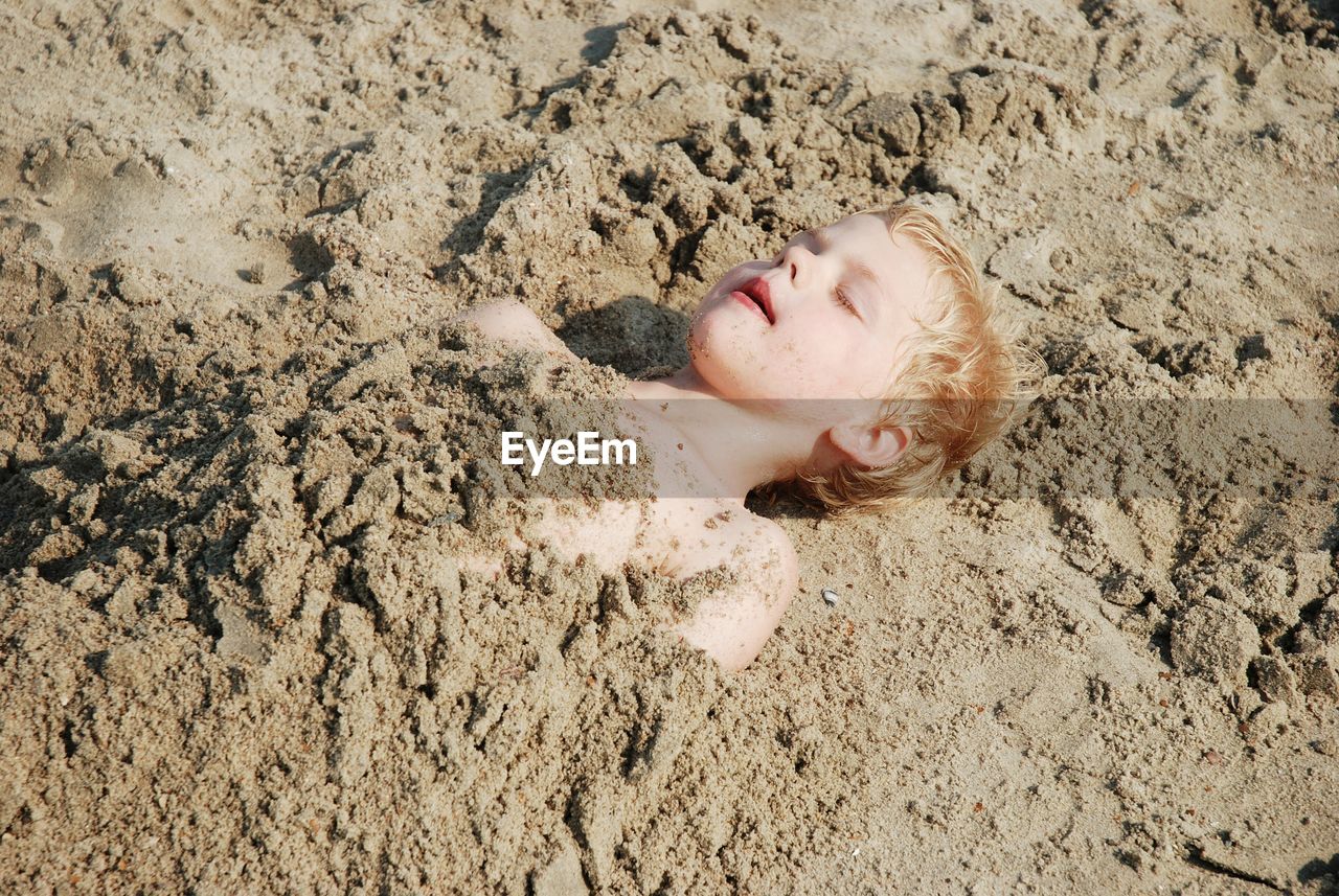 High angle view of boy covered with sand at beach on sunny day