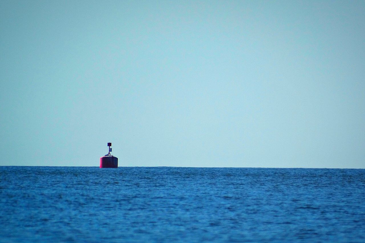 Lighthouse by sea against clear blue sky