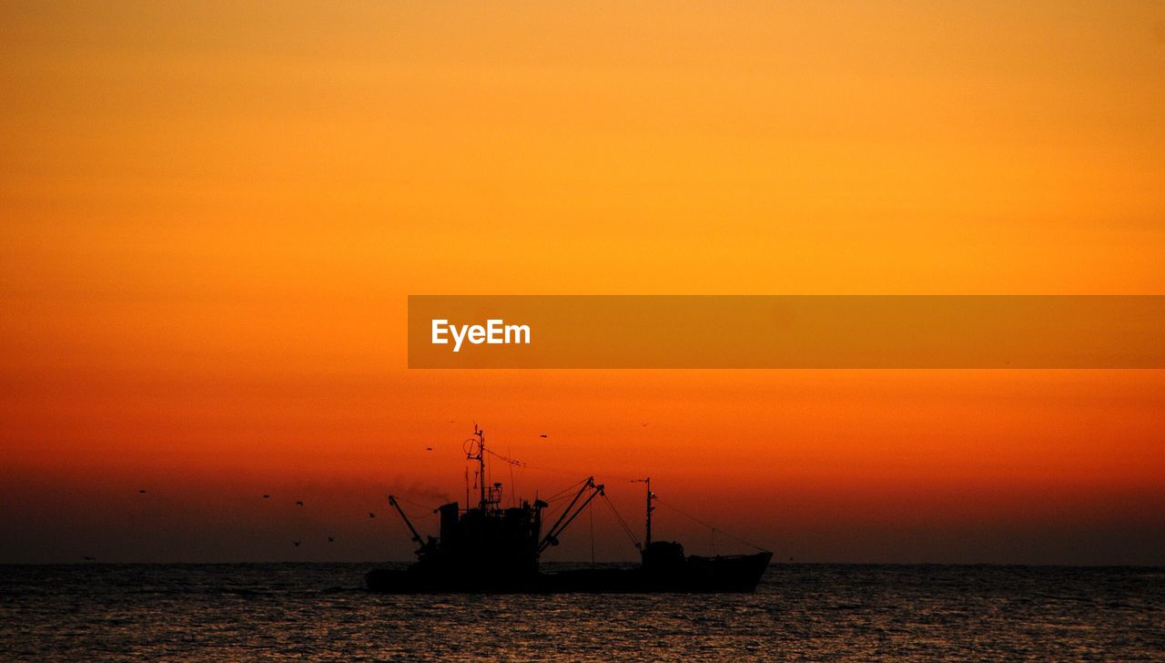 Silhouette ship in sea against orange sky