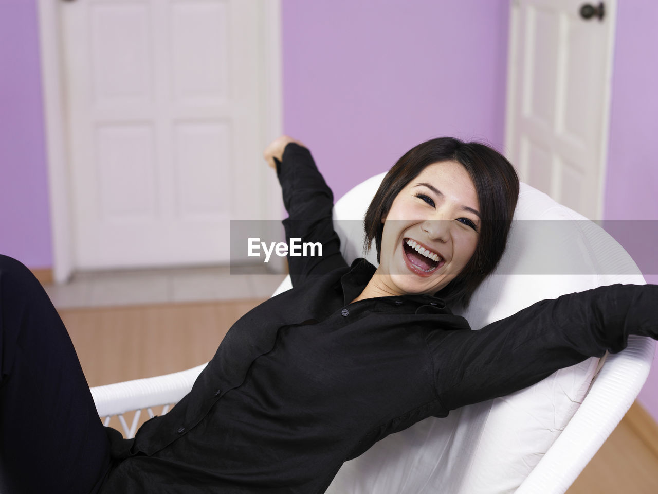 Cheerful woman with arms outstretched sitting on chair at home