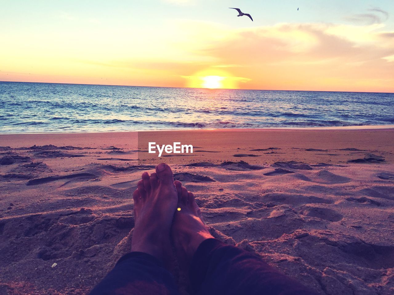 Low section of person sitting on sand at beach