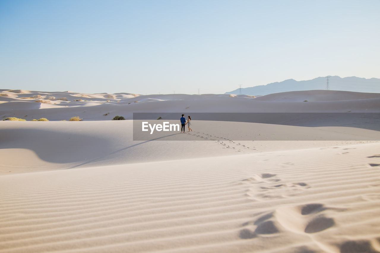 Mid distance view of couple walking on sand at desert against sky