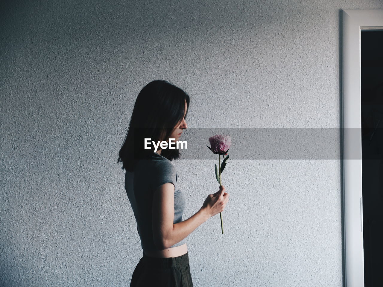 Woman holding flower while standing against wall
