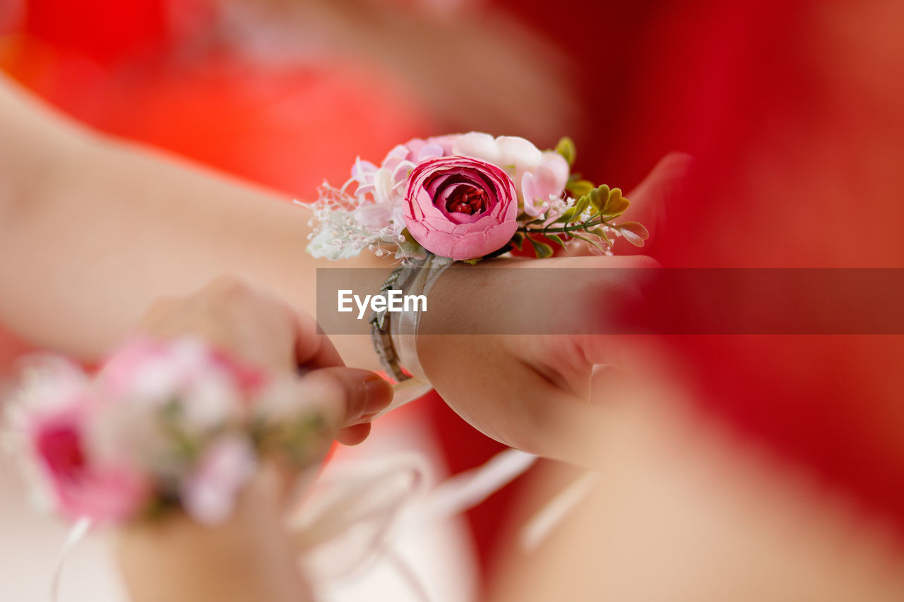 Close-up of woman putting pink flower bracelet on hand