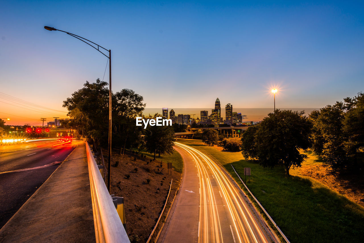 LIGHT TRAILS ON ROAD IN CITY AGAINST SKY