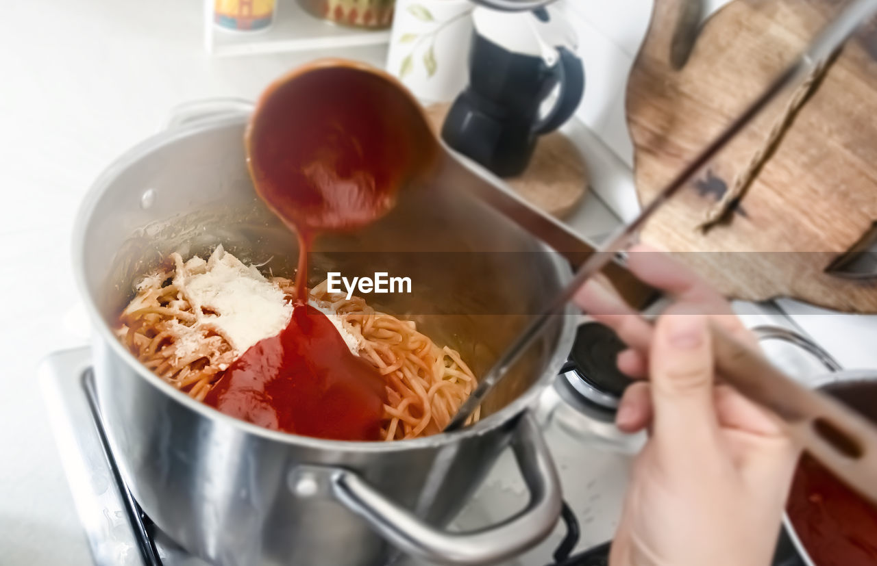 Seasoning a pan full of freshly cooked spaghetti by pouring the tomato sauce with a steel ladle. 