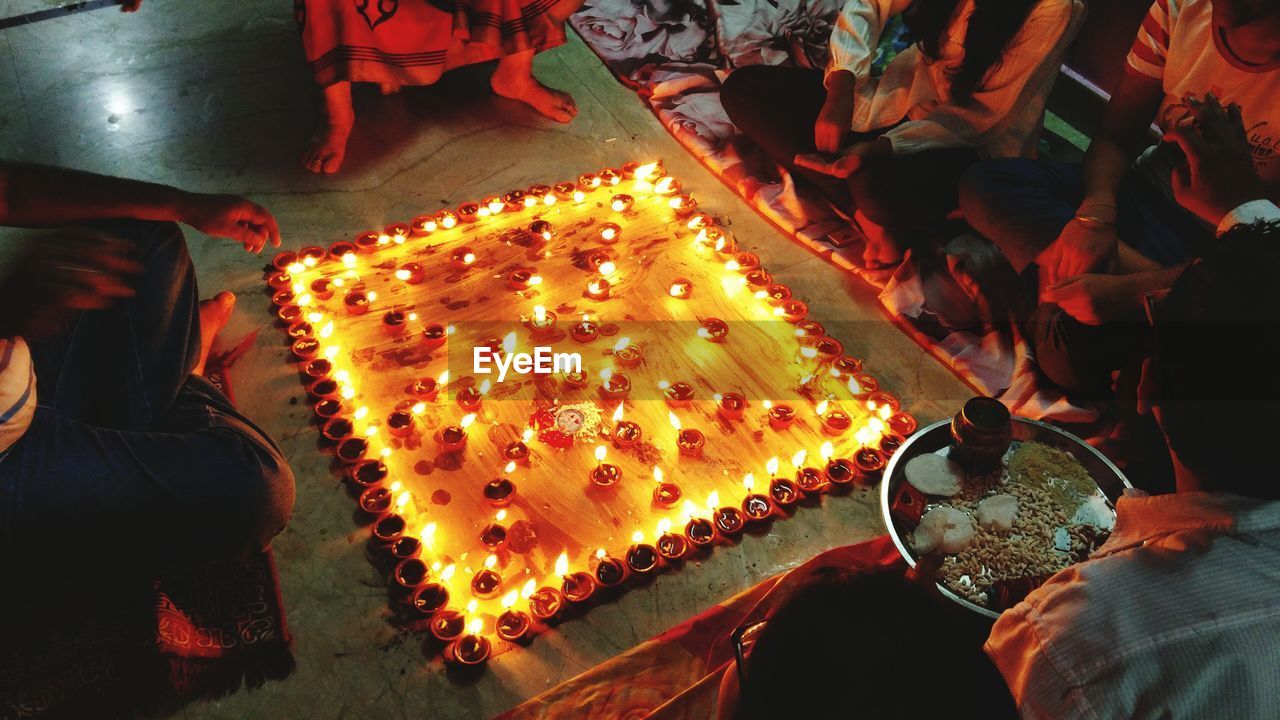 Low section of people sitting around lit diyas on floor