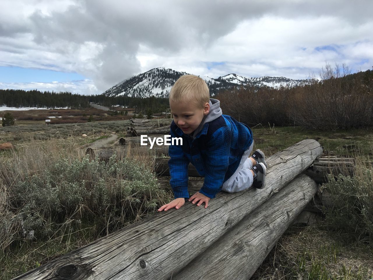 Full length of boy crawling on log at field against sky during winter