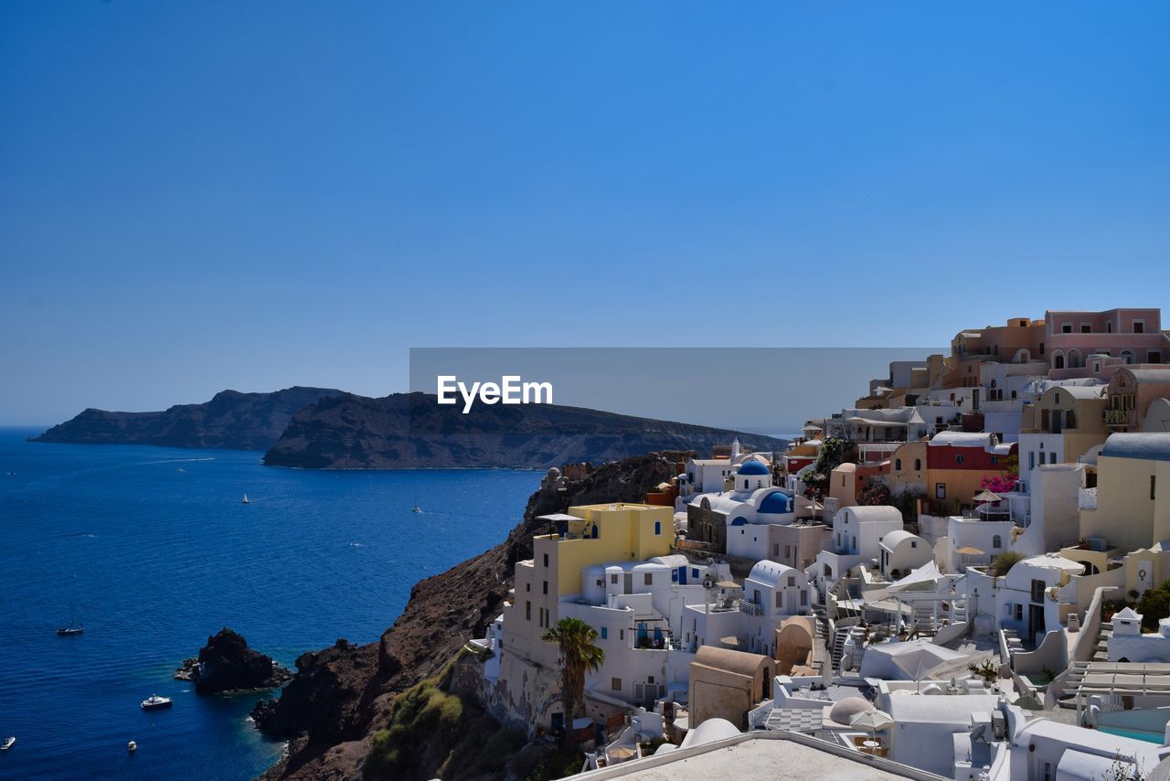 Scenic view of sea by buildings against clear blue sky