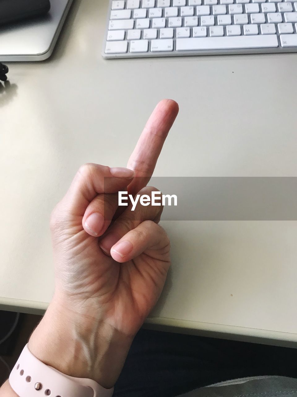 Cropped hand of person showing obscene gesture by keyboard on table