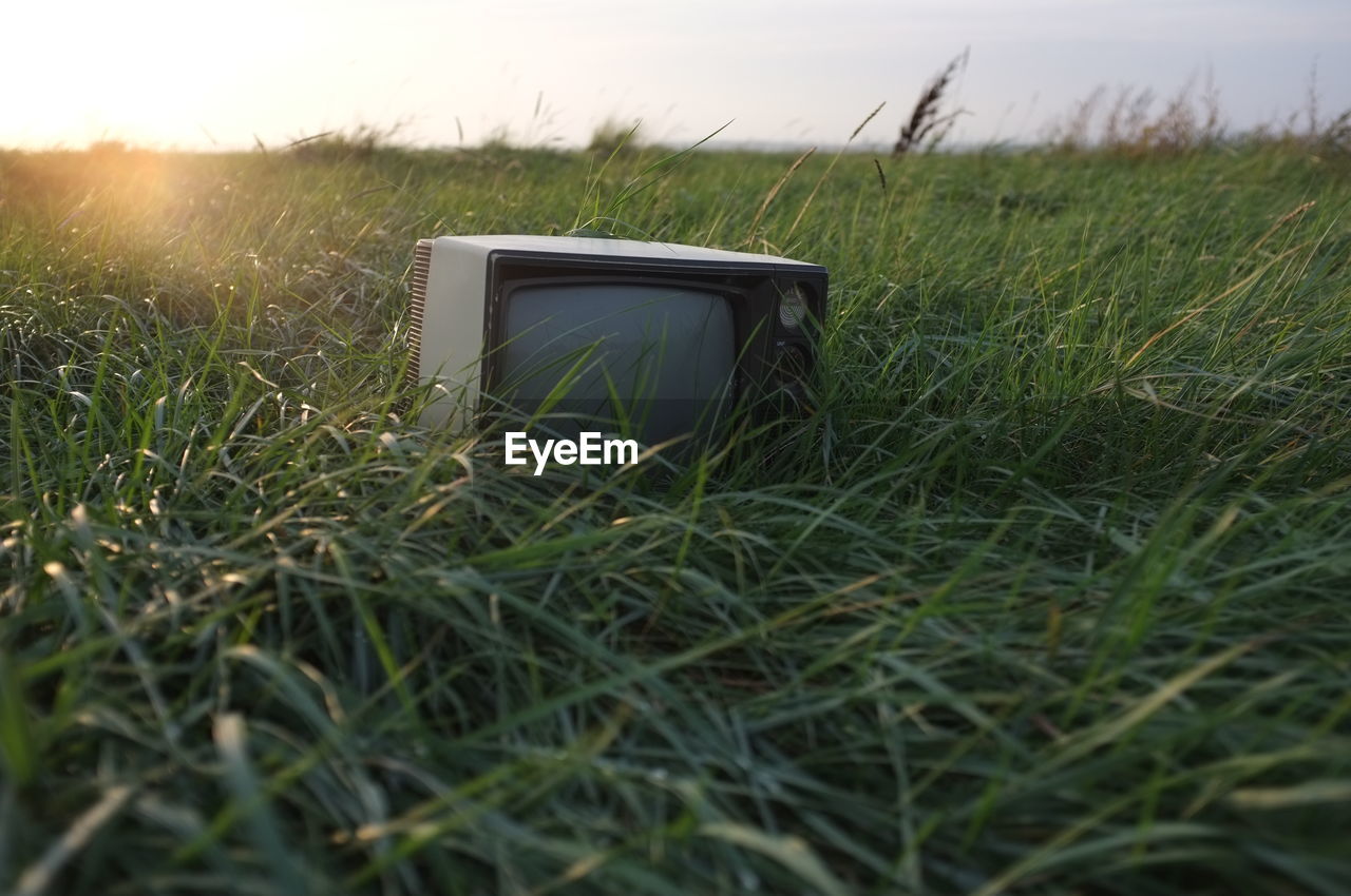 Abandoned television set on grassy field against sky