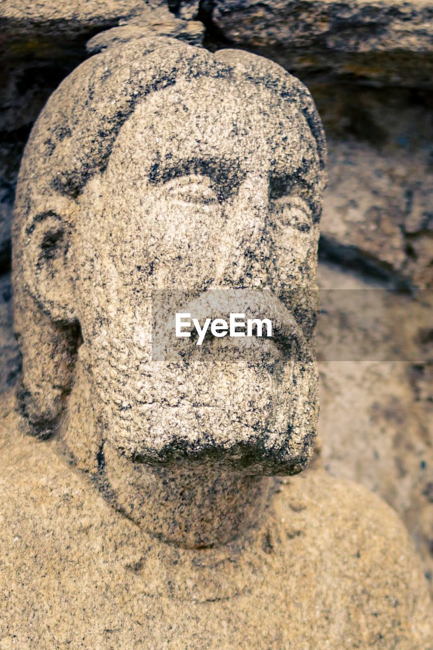 CLOSE-UP OF OLD STATUE AGAINST STONE WALL