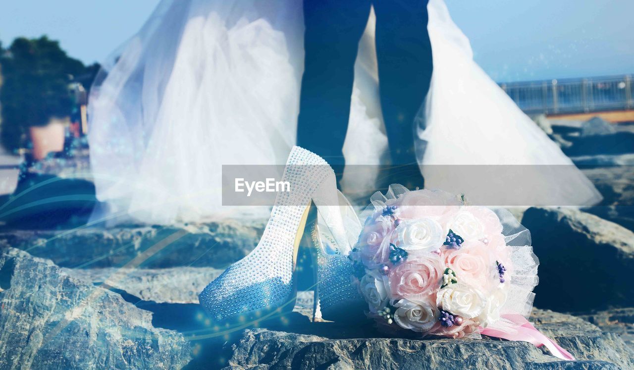 Close-up of rose bouquet and high heels shoes on rock