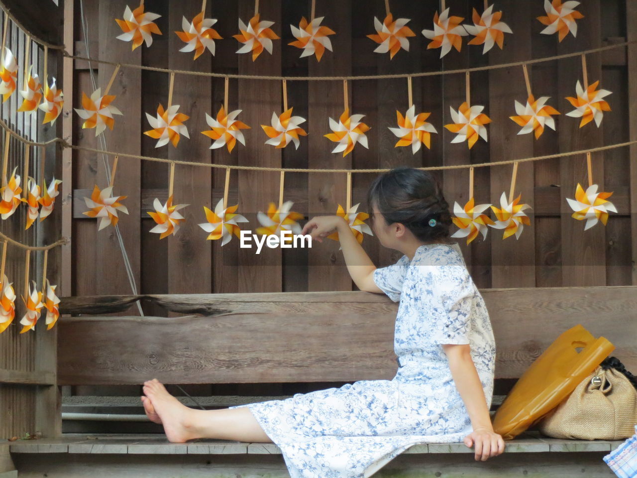 Side view of woman playing with pinwheel decoration sitting on bench