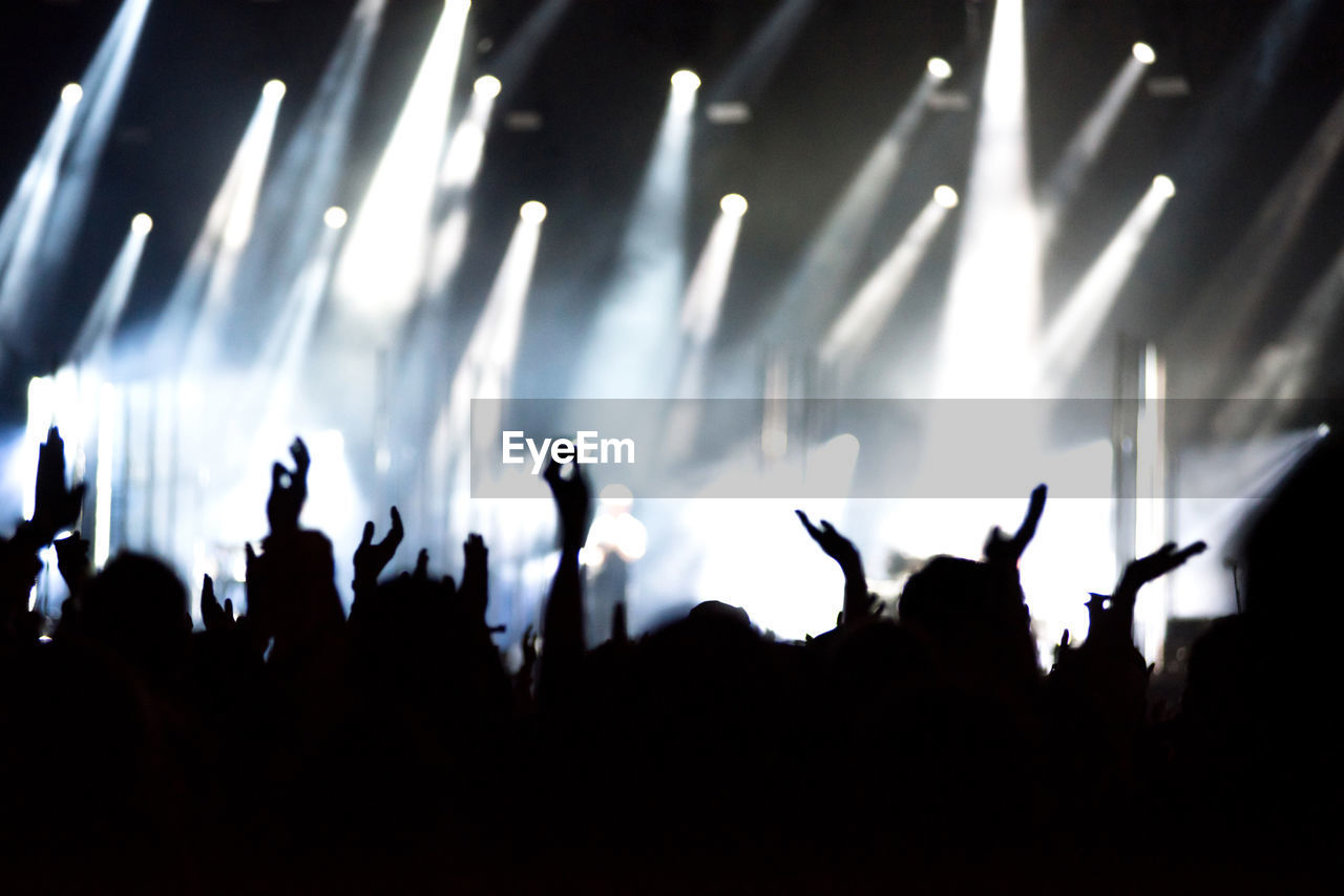 Rear view of silhouette of crowd with arms outstretched at concert. summer music festival concept