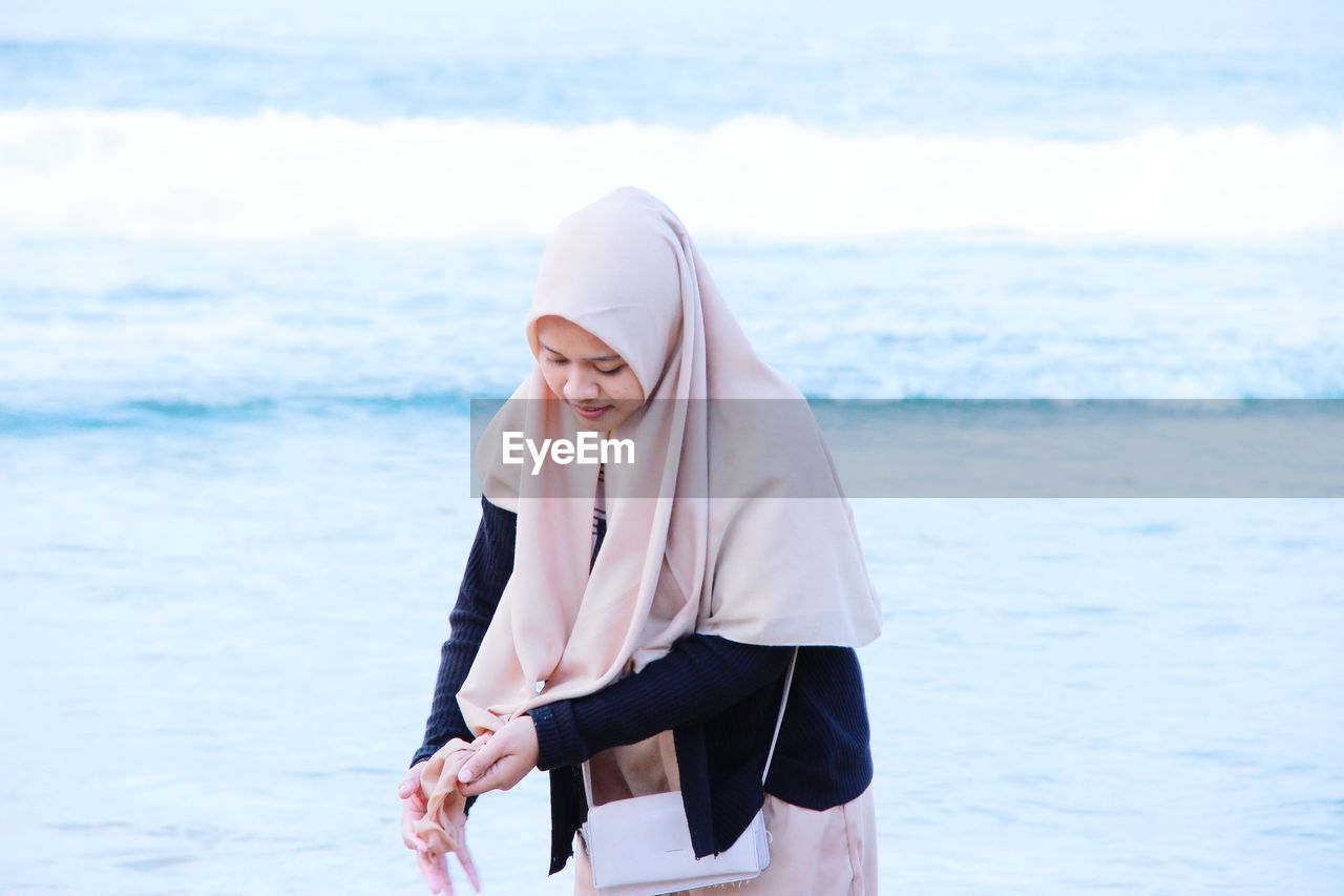 Woman wearing hijab standing against sea
