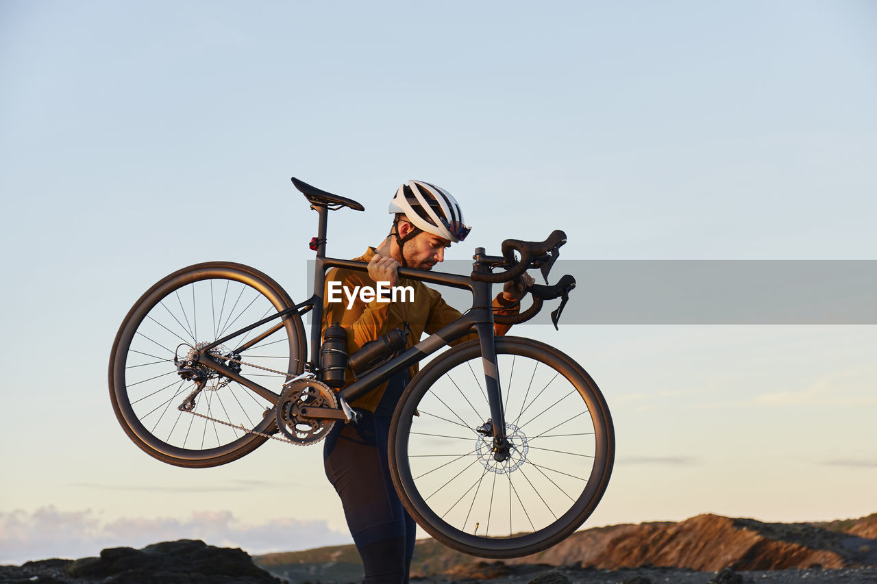 Cyclist carrying bicycle walking in front of sky