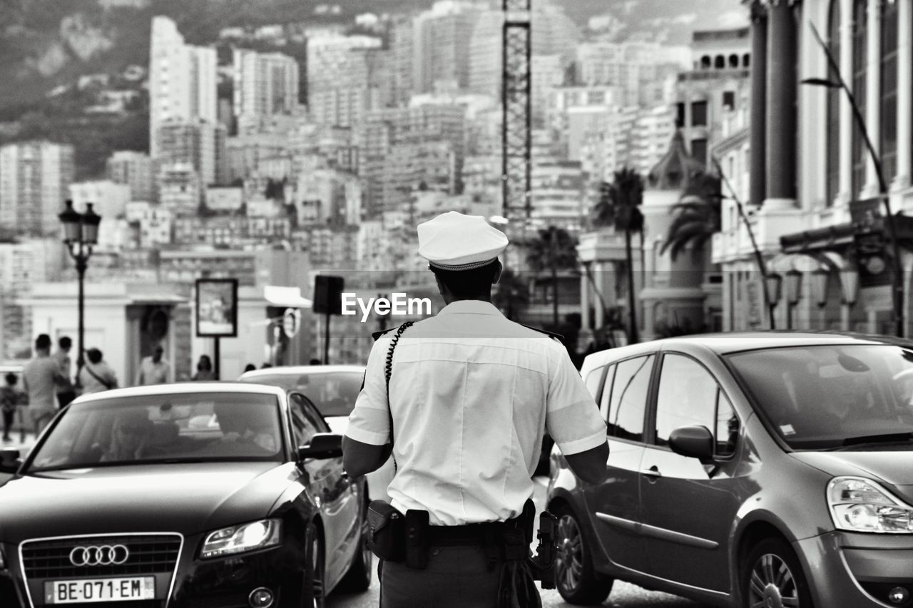 REAR VIEW OF MAN WITH CARS IN CITY