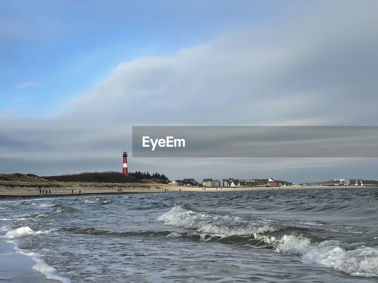 lighthouse by sea against cloudy sky