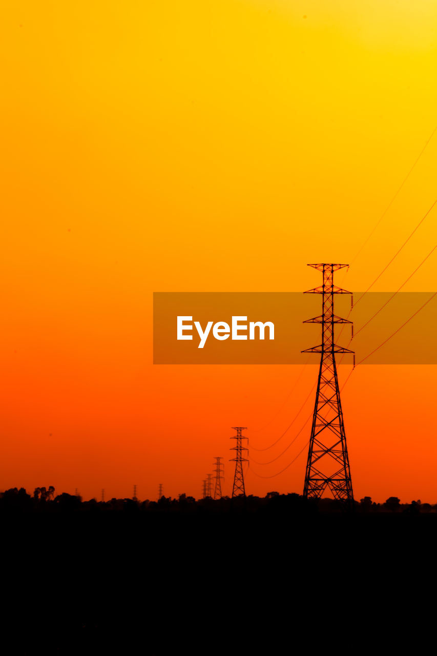 Silhouette electricity pylon against orange sky