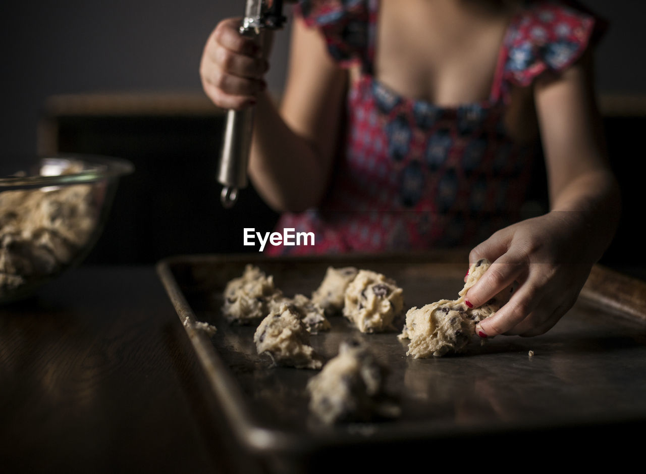 Midsection of girl placing batter on baking sheet at home