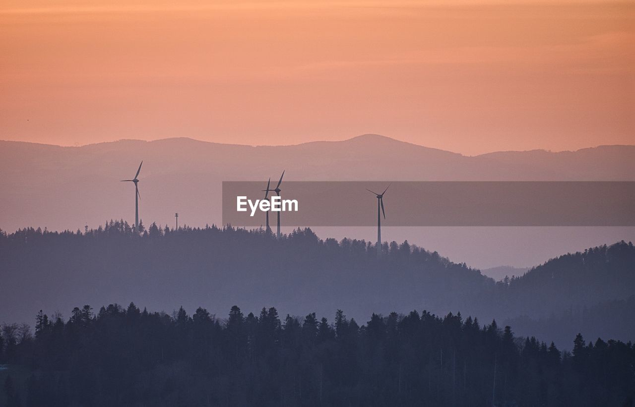 Scenic view of silhouette mountains with wind power plant against sky during sunset