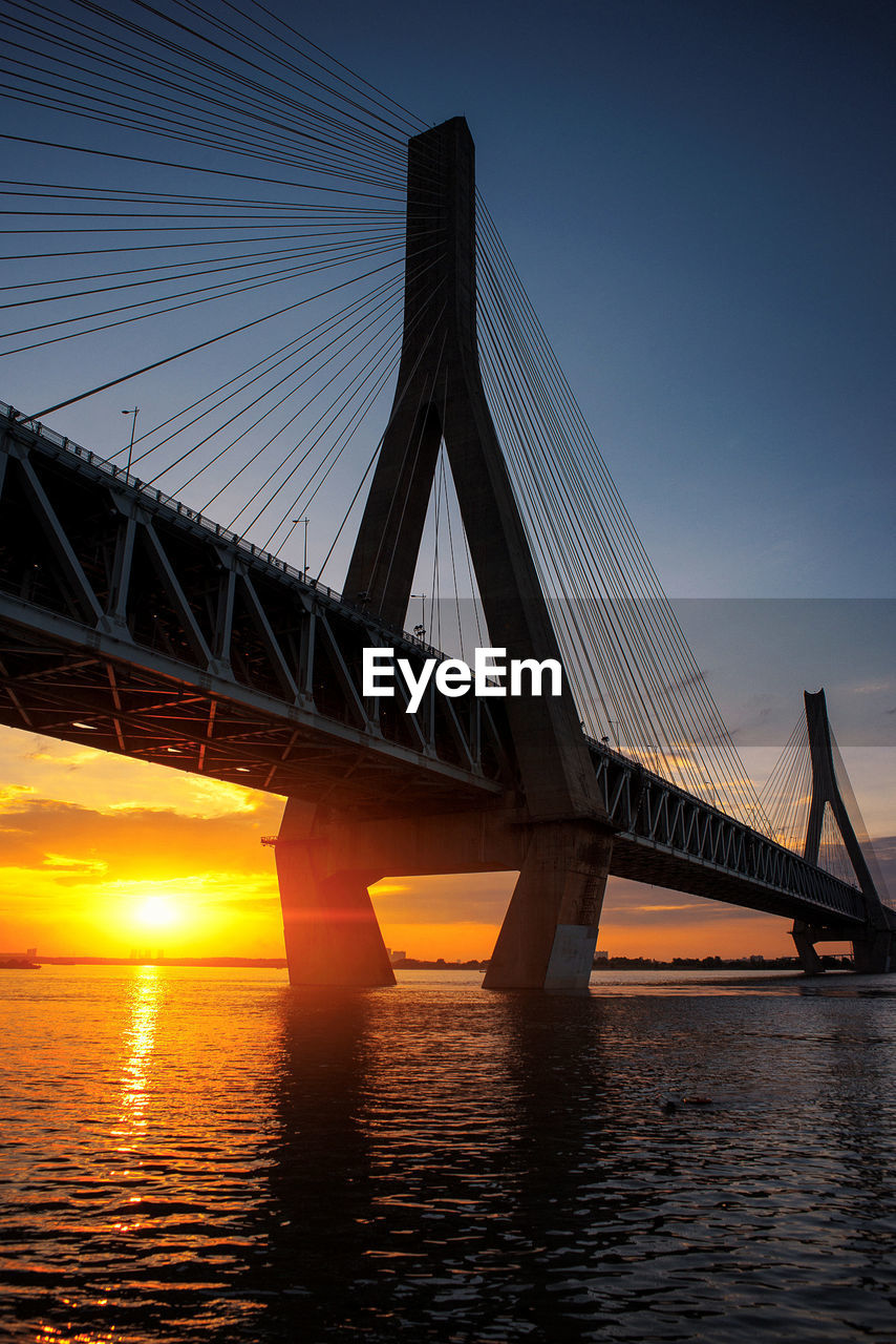 Cable-stayed bridge over river during sunset