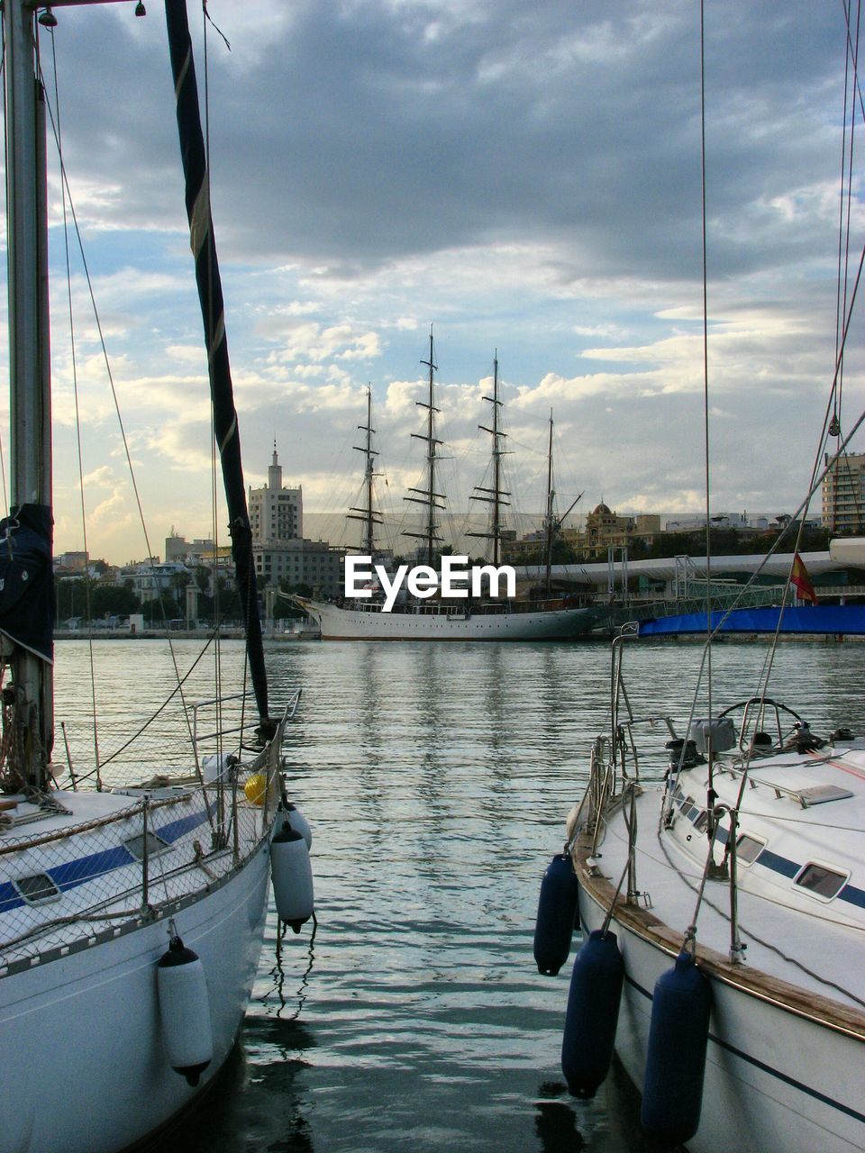 SAILBOATS MOORED ON RIVER IN CITY AGAINST SKY