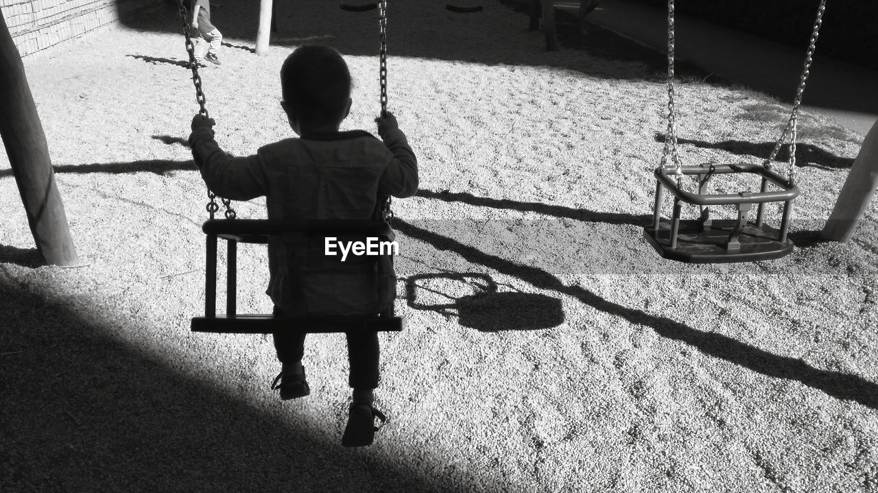 Rear view of boy sitting on swing at playground