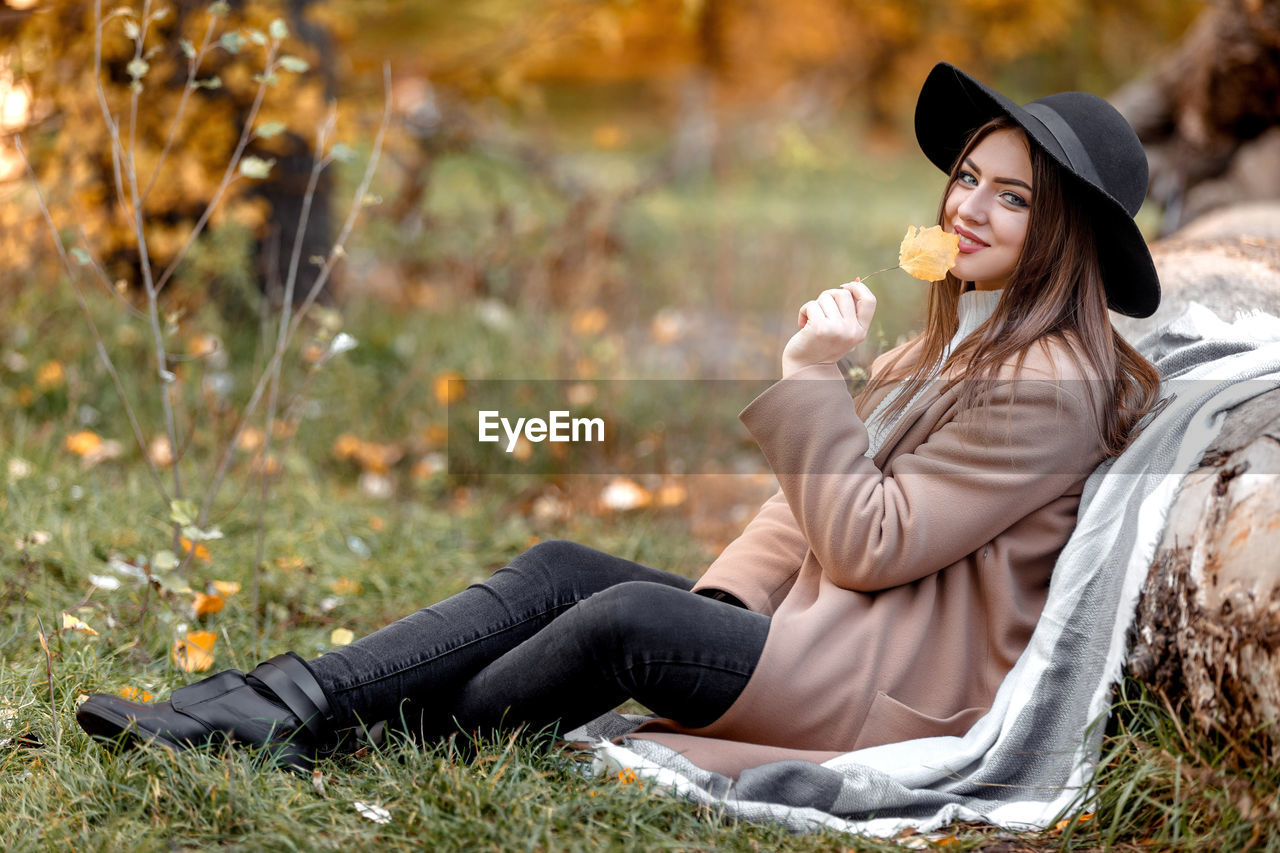 Portrait of young woman leaning wooden log at park