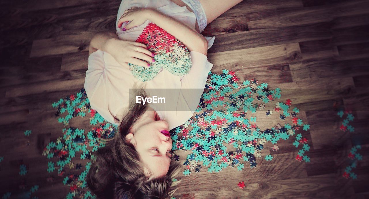High angle view of woman lying down amidst jigsaw pieces on hardwood floor