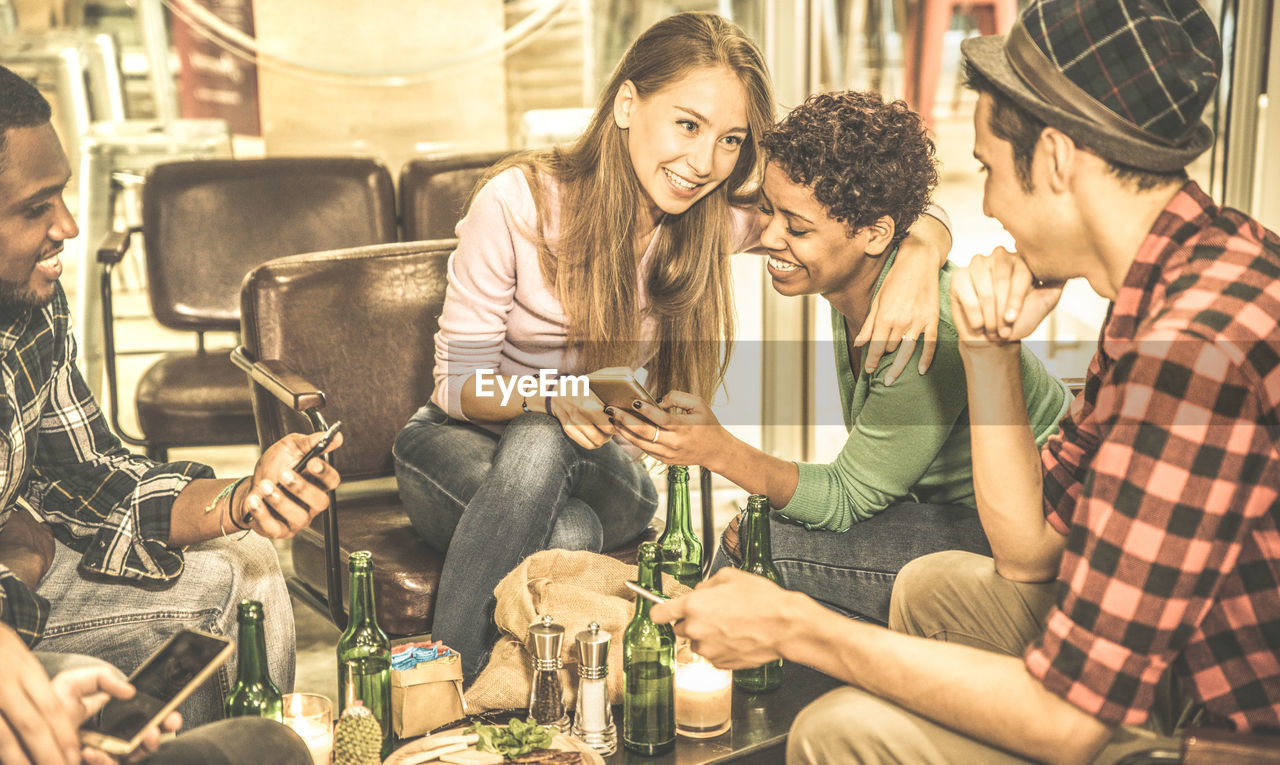 Smiling friends using phones while sitting in restaurant