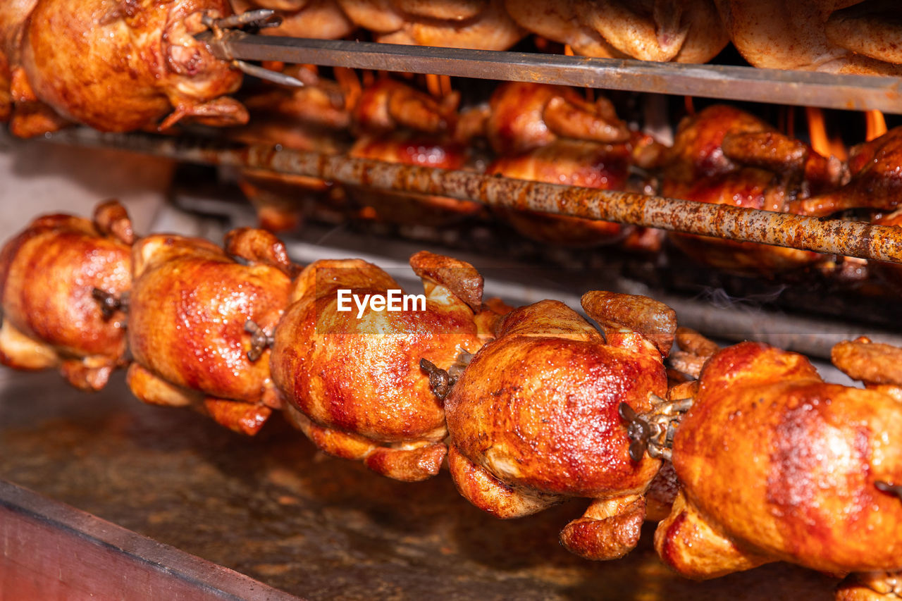 Multiple chickens cooking on a rotisserie spit, crispy and golden, in a commercial kitchen