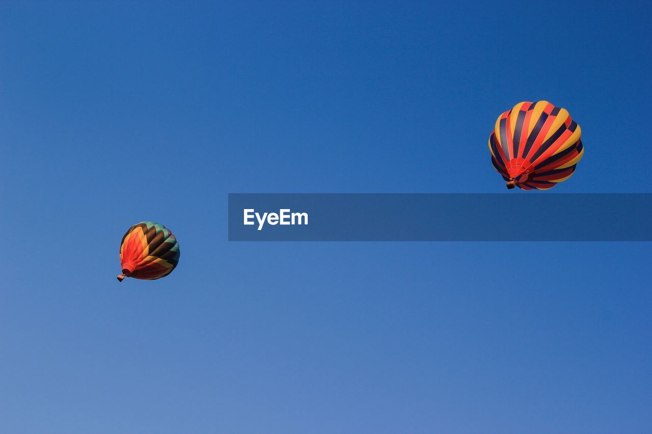 Low angle view of hot air balloons against clear blue sky on sunny day