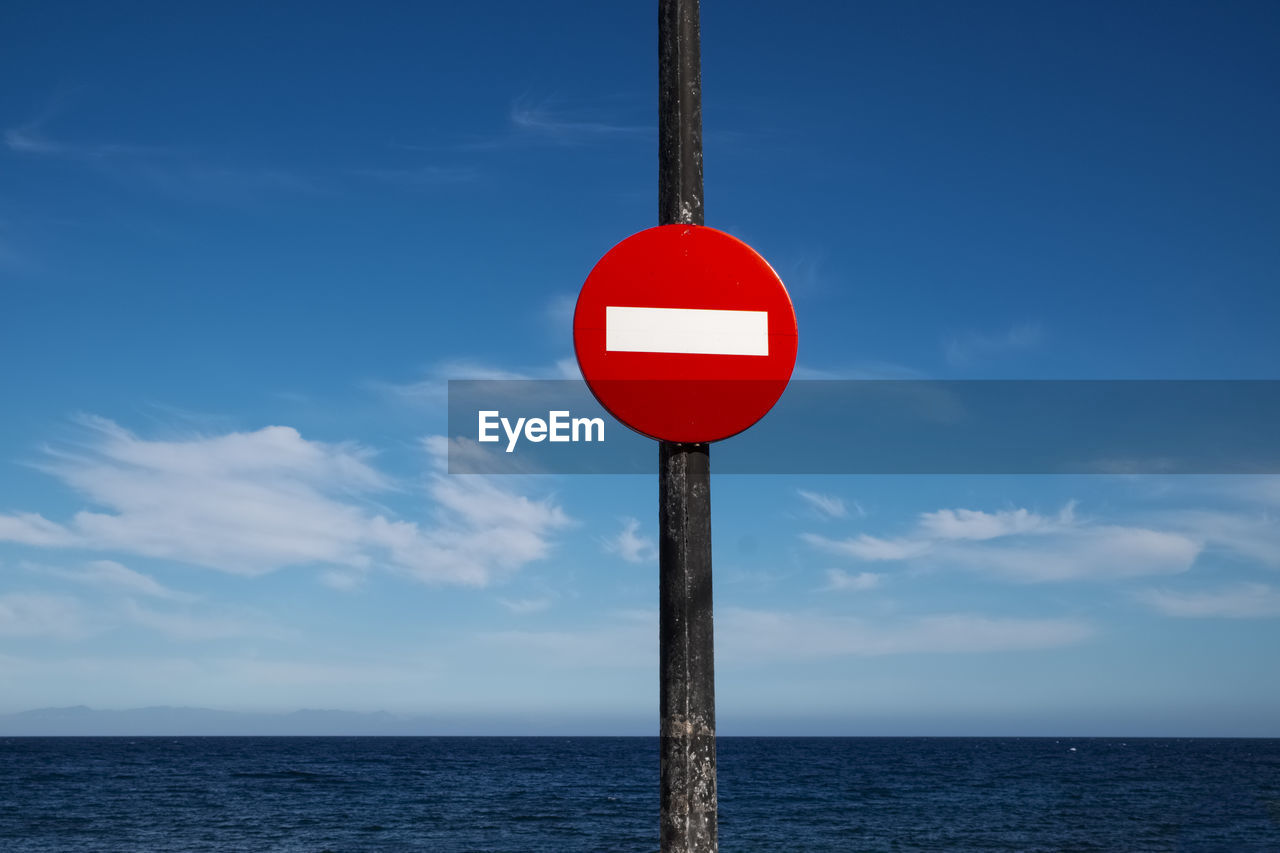 Road sign by sea against sky