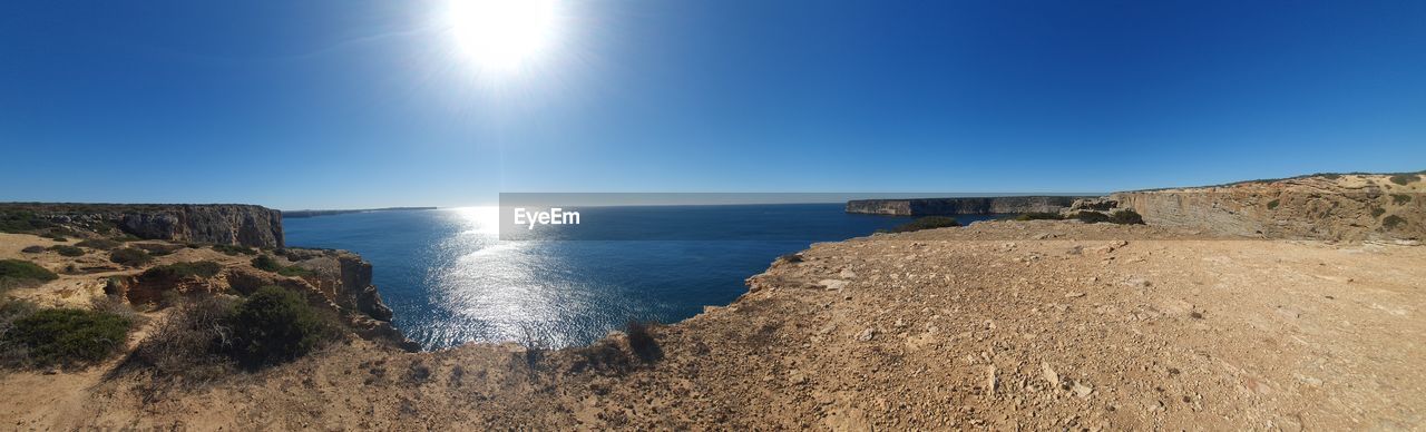 water, sky, sea, land, scenics - nature, nature, coast, beach, cliff, horizon, landscape, terrain, beauty in nature, blue, sunlight, environment, rock, no people, shore, clear sky, ocean, sun, body of water, tranquility, horizon over water, outdoors, travel destinations, mountain, tranquil scene, travel, coastline, sunny, day, sand, tourism, non-urban scene, panoramic